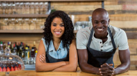 Portrait of smiling waiter and waitress leaning at counter in café
